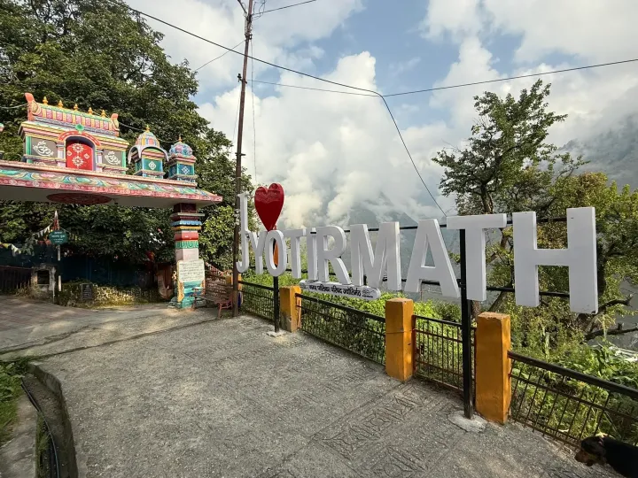 The Jyotirmath sign and a colourful temple gateway in Joshimath under a cloudy sky