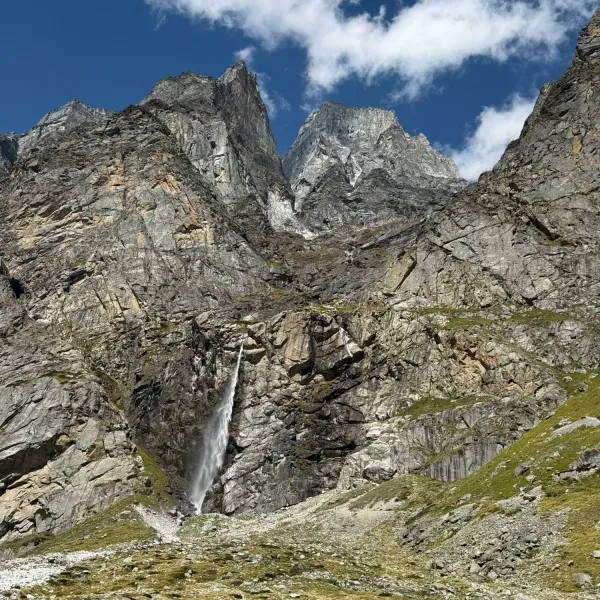 The Vasudhara waterfall falling in a single thread from the cliffs above a green alpine meadow
