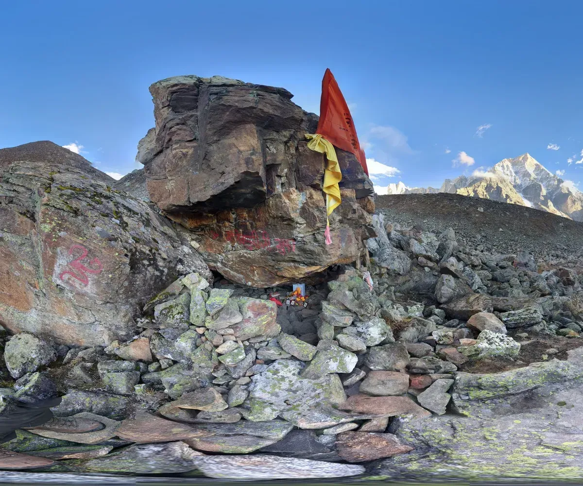 A 360-degree panorama of Sri Devpuriji's cave: a boulder shrine with an orange flag and Om sign among snow peaks