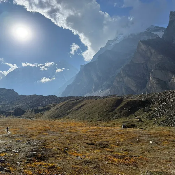 The golden meadow of the Chakratirth valley in low sunlight beneath rock walls