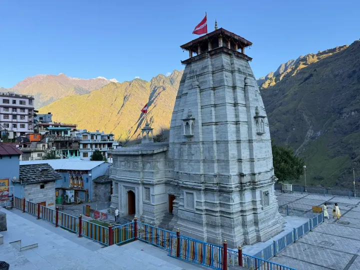 The stone shikhara of Narsingh Temple in Joshimath with a red flag, mountains lit by evening sun behind