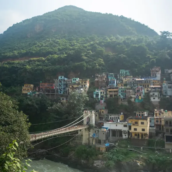 Colourful houses on a wooded hillside above the Ganges with a suspension footbridge at Rishikesh