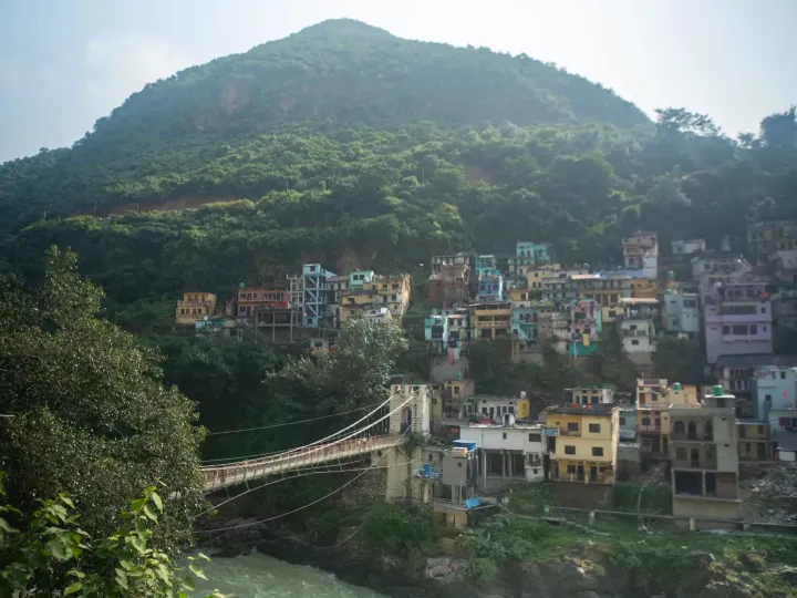 Colourful houses on a wooded hillside above the Ganges with a suspension footbridge at Rishikesh
