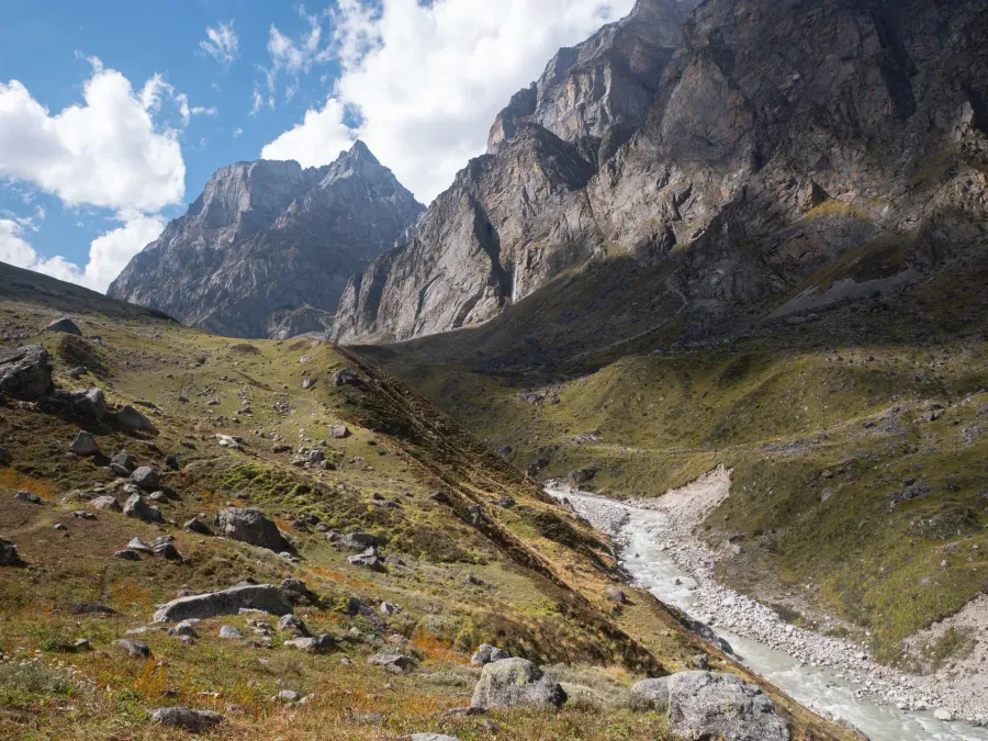 Green Himalayan valley with a glacier river below rocky peaks and a waterfall