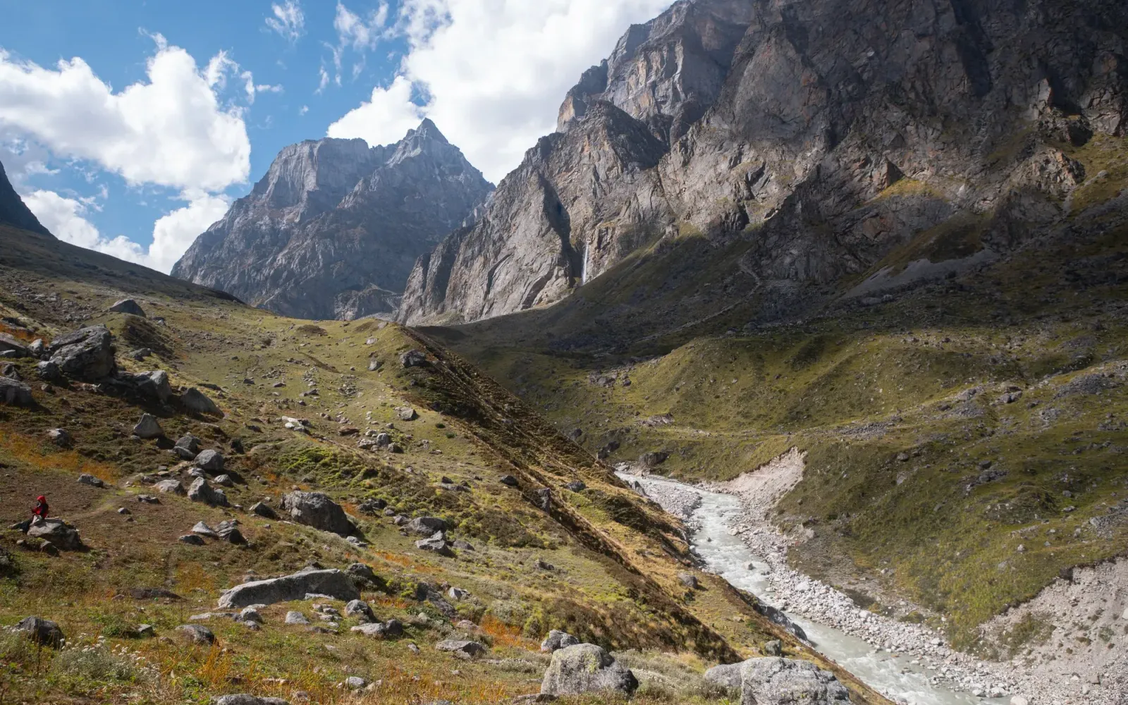 Green Himalayan valley with a glacier river below rocky peaks and a waterfall