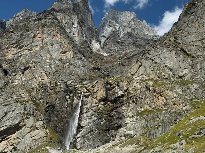 The Vasudhara waterfall falling in a single thread from the cliffs above a green alpine meadow