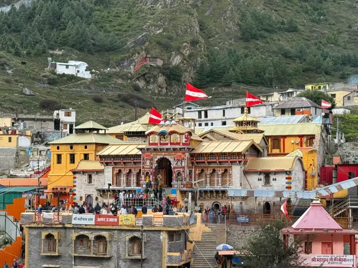 The colourfully painted facade of Badrinath Temple with red flags and pilgrims on the steps