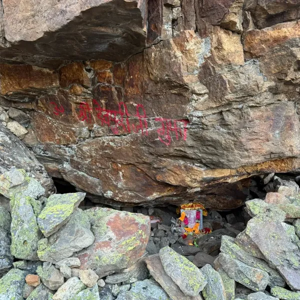 The rock of Sri Devpuriji's cave with its name painted in red Devanagari and a small shrine with flowers