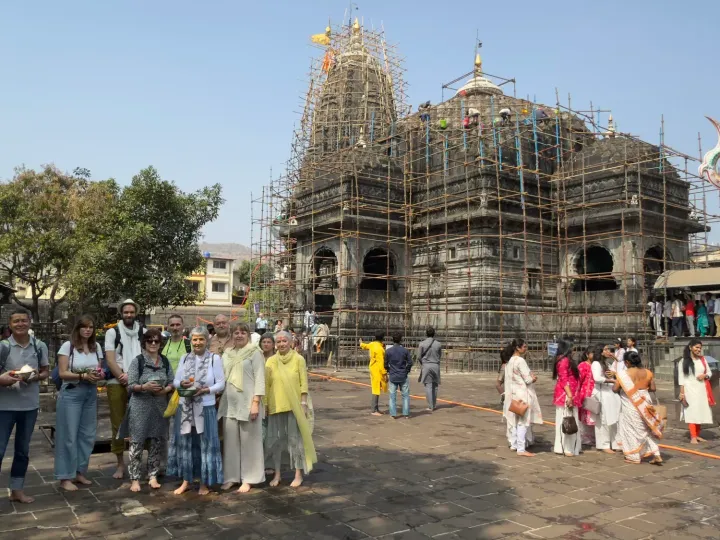 Pilgrims gathered in front of the Trimbakeshwar temple under scaffolding, with a painted trident beside it