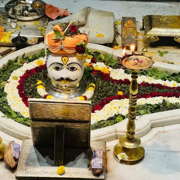 A silver Shiva mask on a lingam surrounded by flowers and oil lamps in Trimbakeshwar